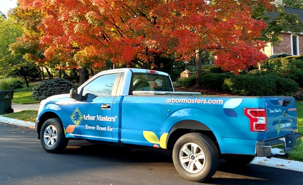 Arbor Masters service truck parked by a vibrant red maple during fall tree care in Cedar Rapids.