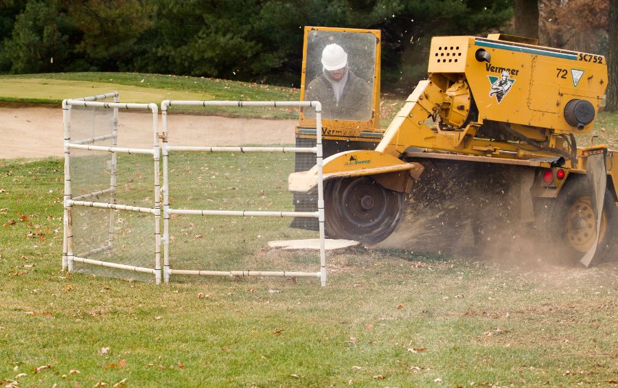 Arbor Masters grinding a large stump, with a protective barrier in place to prevent home damage caused by projectiles.