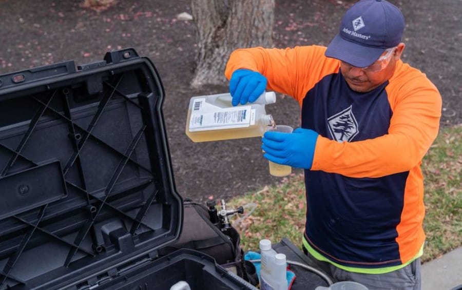 Arbor Masters plant health care technician wearing safety glasses and gloves measuring fungicide into a calibrated container for application.