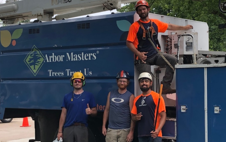 Several Arbor Masters team members pose in various levels on company-branded bucket truck demonstrating readiness for tree services throughout Des Moines.