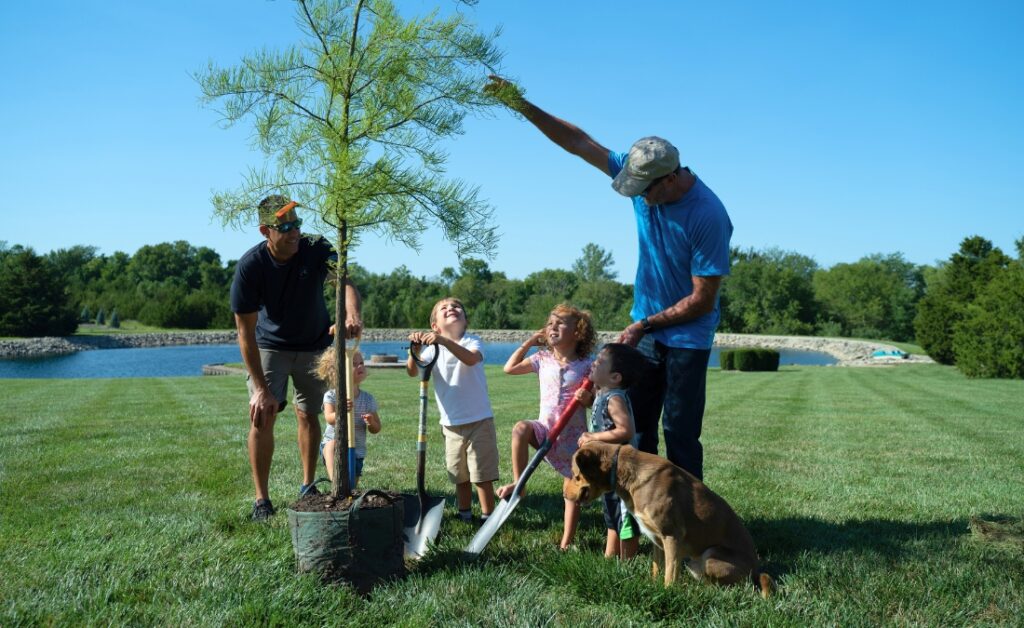 Arbor Masters tree care professionals planting young tree with family and children in Quad Cities waterfront location.