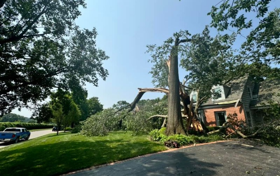 Storm-damaged tree fallen on brick house in Quad Cities requiring emergency tree removal services.