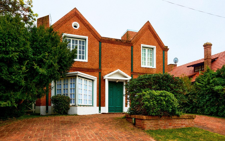 Red brick Tudor-style home with professionally trimmed evergreen trees and manicured shrubs flanking the front entrance.
