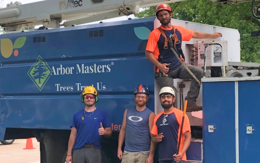 Arbor Masters tree care crew wearing safety helmets standing in front of blue bucket truck with company logo.