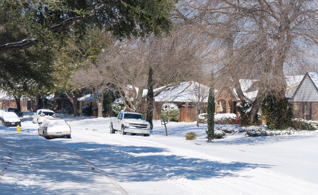 A Fort Worth residential neighborhood covered in snow with mature trees lining the street and houses with snow-covered roofs.