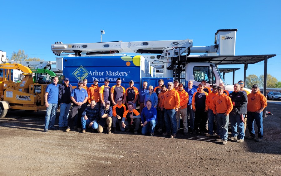 The Arbor Masters crew wearing blue and orange and standing in front of a blue bucket truck with the Arbor Masters branding.