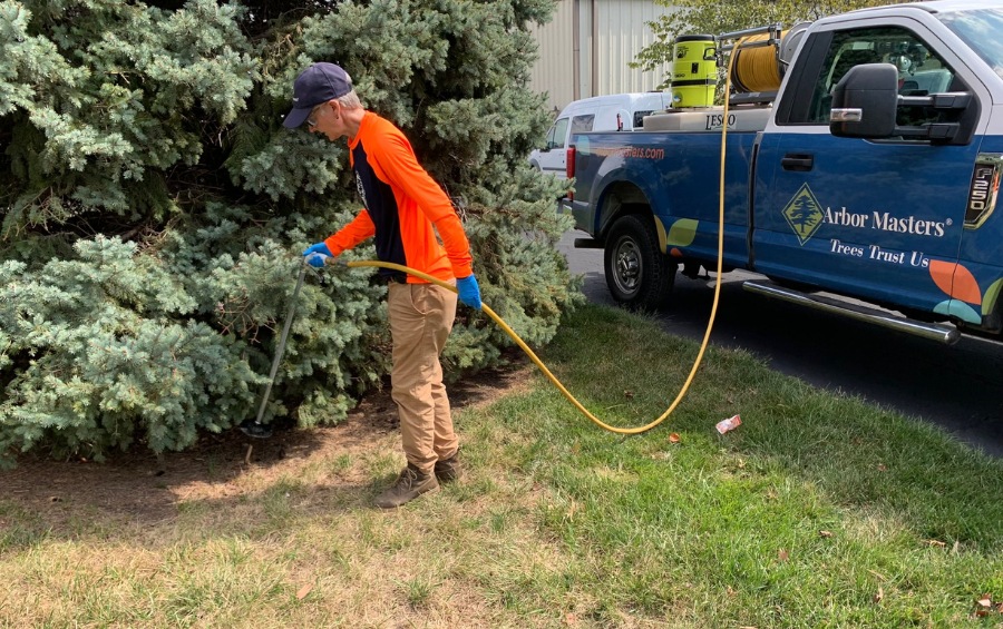 Arbor Masters technician performing deep root fertilization with subsurface injection equipment next to a branded company truck on a residential property.