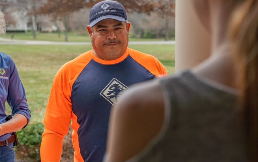 An Arbor Masters technician in branded gear speaks with a homeowner during a property visit.