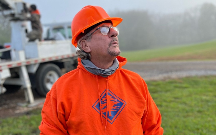 An Arbor Masters arborist in a blue shirt and orange hard hat measures a mature tree trunk with a diameter tape in a residential yard.