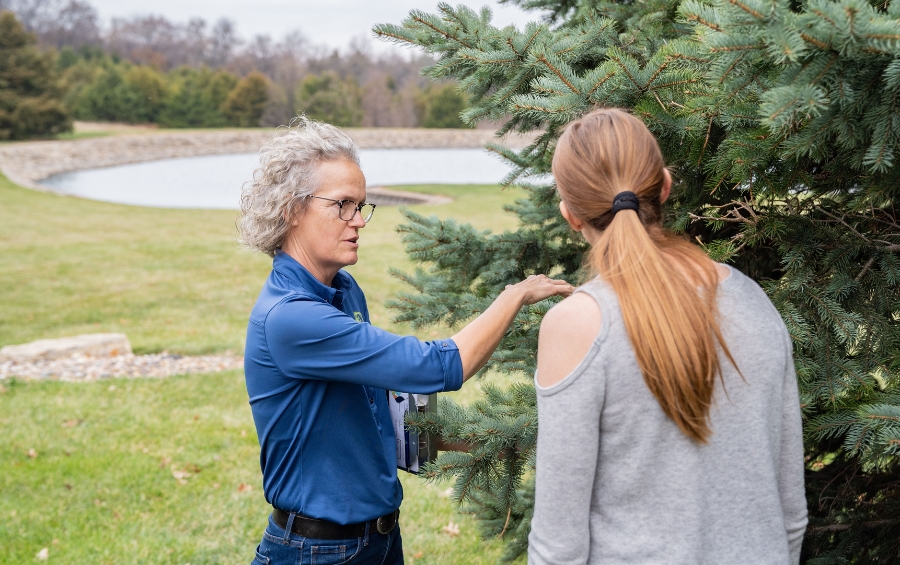 An Arbor Masters Certified Arborist explaining tree structural concerns to a Wichita homeowner during a winter assessment consultation, pointing out specific areas needing attention on an evergreen tree