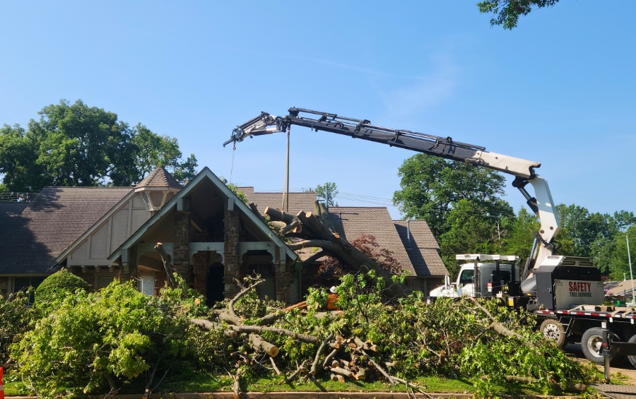 The Arbor Masters crane removing large tree debris from storm-damaged house in Wichita neighborhood after severe wind event.