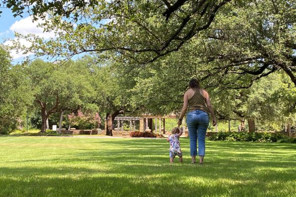 Mother and child walking hand in hand in a manicured lawn and landscape with trees on a property