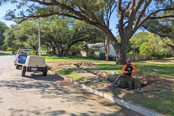 A guy building a trech and air spaiding the roots of a tree on a property in Catoosa, OK