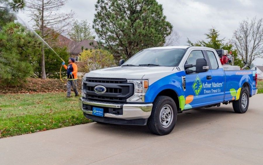 Arbor Masters truck and technician providing preventive tree care treatment at a residential property.
