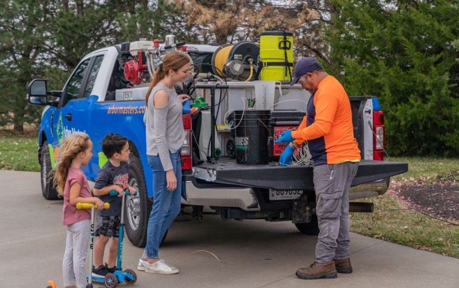 Arbor Masters arborist speaking with a homeowner and two children beside a plant health care service truck.
